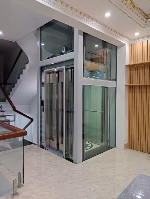 Thang máy lồng kính khung trắng cạnh cầu thang nhà phố